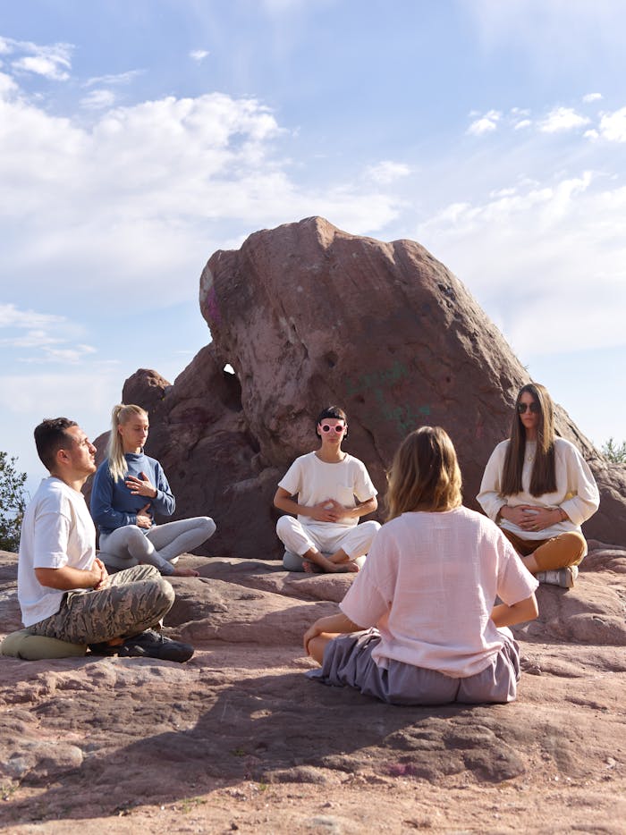 A group of adults meditating outdoors on a rocky landscape under a clear sky.